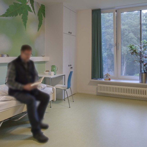 Ein Mann sitzt auf einem Bett ineinem Patientenzimmer und liest eine Broschüre