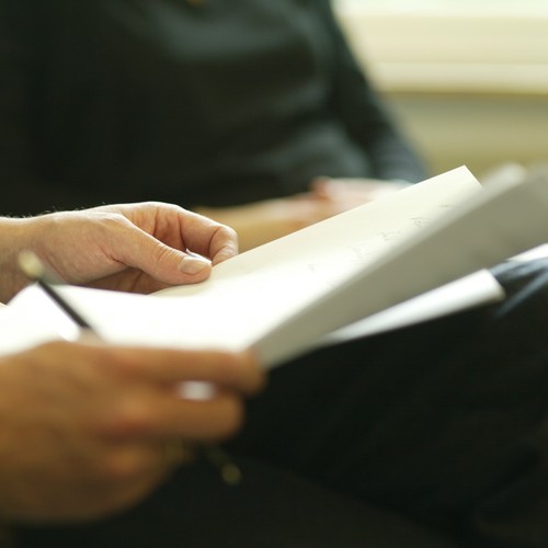 Zwei Hände haltern ein Schriftstück und einen Schreibstift.